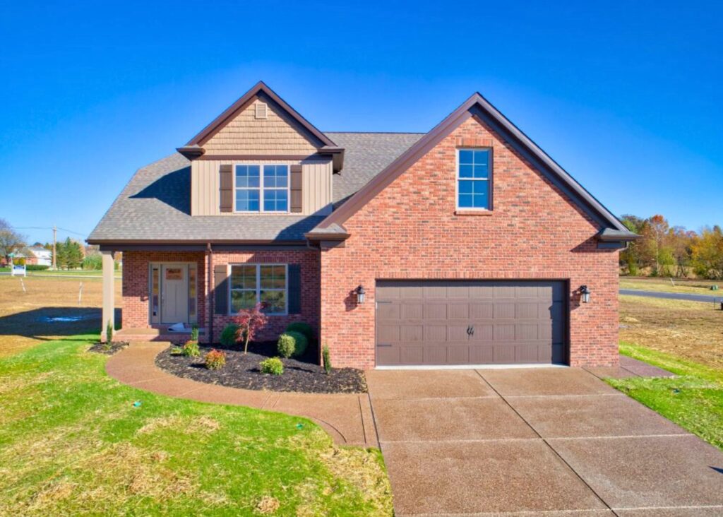 Two-story suburban house by John Elpers with a brick and siding exterior, attached two-car garage, front porch, landscaped yard, and a clear blue sky in the background.