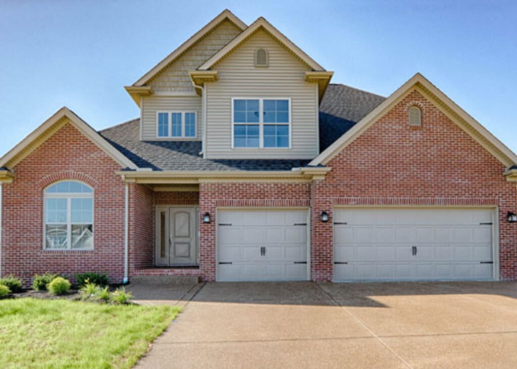 Two-story suburban house by John Elpers with red brick and beige siding, featuring three gray garage doors and multiple windows, set on a concrete driveway with a small, neatly landscaped front yard.