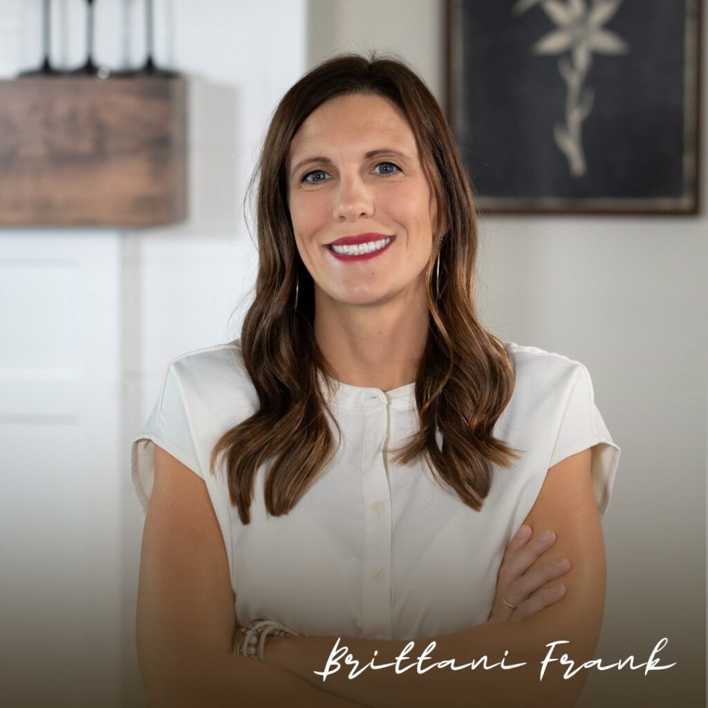 Smiling brunette woman in a white blouse poses with folded arms indoors, conveying warmth and confidence; “Brittany Frank” appears below.